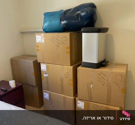 ארגזים מסודרים בחדר עם מזרן וארון קטן